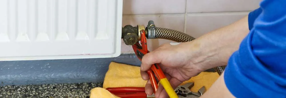 Eine Person arbeitet mit einer Rohrzange an einem Ventil eines Heizkörpers.